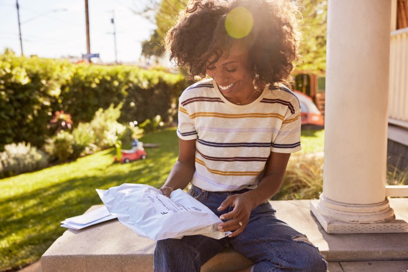 Woman sitting outside smiling at mailed package