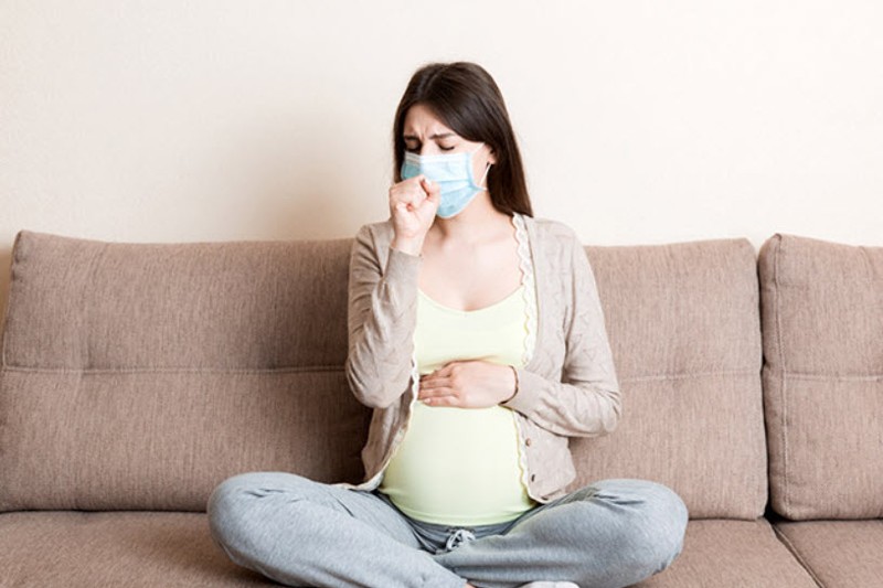 Pregnant woman with mask on coughing