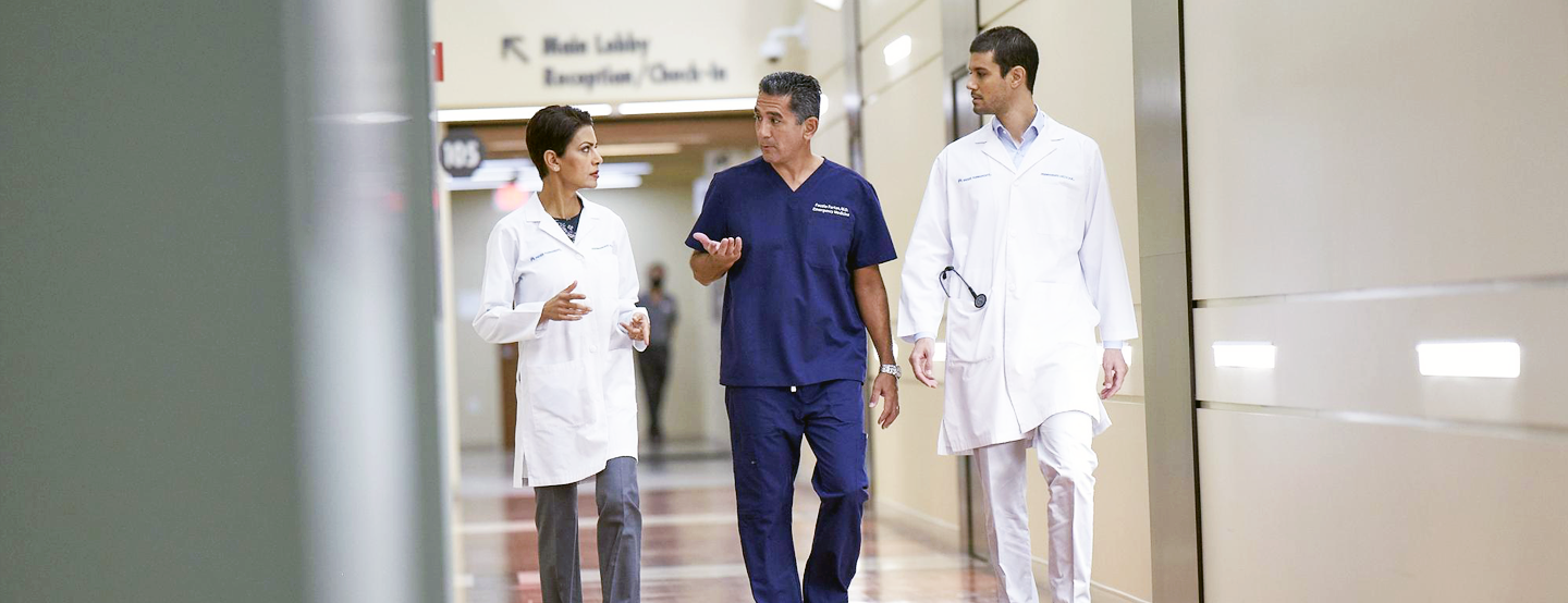 Three Permanente physician confer with each other as they walk down the hallway of a medical facility.